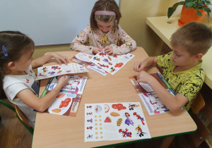 Dzieci uzupełniają kartę pracy naklejkami.