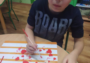 Chłopiec maluje serduszka farbą.