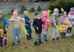 Powitanie wiosny w ogrodzie- dzieci trzymają kolorowe gałązki z bibuły.