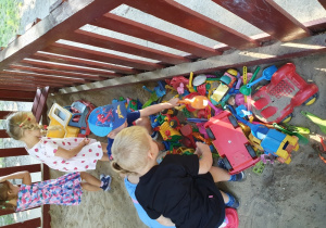 Dzieci oglądają zabawki w piaskownicy.
