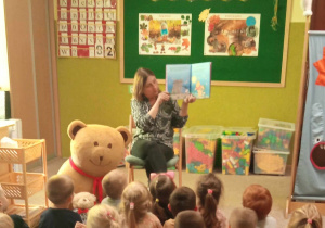 Dzieci oglądają ilustracje w książce, którą czyta pani dyrektor.
