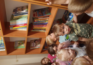 Dzieci oglądają regały z książkami w przedszkolnej bibliotece.