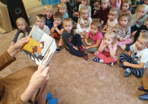 Dzieci słuchają opowiadania czytanego przez zaproszonego gościa z Uniwersytetu Trzeciego Wieku.