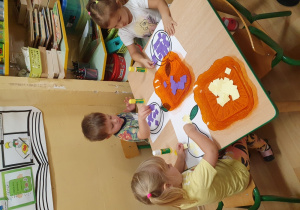 Dzieci wypełniają kontury śliwki kolorowymi kartonikami.