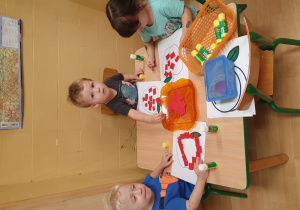 Dzieci wypełniają kontury jabłka kolorowymi kartonikami.