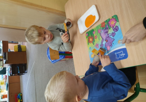 Dzieci malują rolkę od papieru na pomarańczowo.