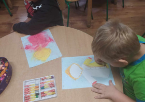 Dzieci kolorują kredkami jesienny płaszczyk.
