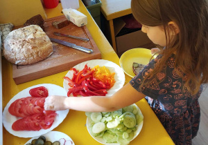Dziewczynka nakłada wybrane warzywo na kromkę chlebek.