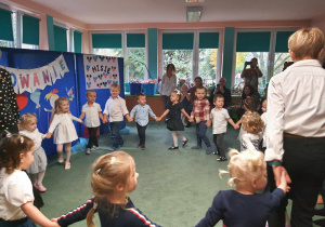 Dzieci z nauczycielkami tańczą w kole.