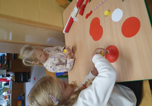 Dzieci przyklejają koła białe i czerwone tworząc kotyliony.
