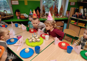Dzieci przy urodzinowym stole dmuchają świeczki.