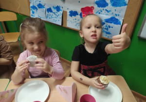 Dzieci przy stole degustują słodkie babeczki.