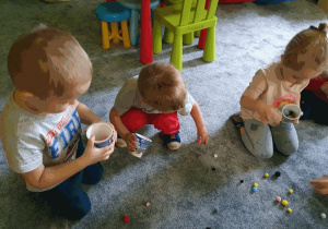 Dzieci zbierają do kubeczka pompony - ćwiczenia usprawniające prace palców.