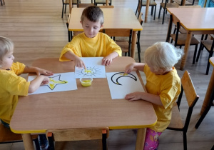 dzieci w żółtych koszulkach stemplują paluszkami kolorowankę