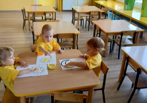 dzieci w żółtych koszulkach stemplują paluszkami kolorowankę