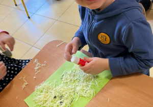 Dzieci wykonują pracę plastyczną, wyklejają postać misia włóczką.