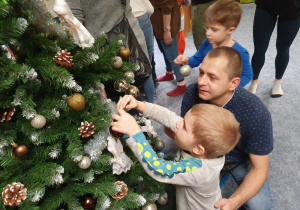 Chłopiec z tatą zawiesza ozdoby na choince.