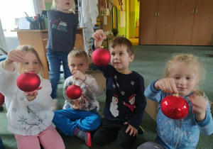 Dzieci z bombkami ozdabiają choinkę klasową.