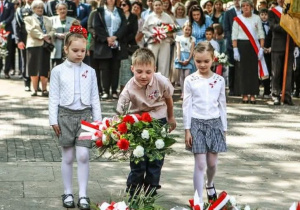 Dzieci składają kwiaty pod pomnikiem Tadeusza Kościuszki.