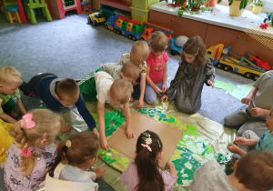 Dzieci wyklejają liść z kartonu wydziaranką.