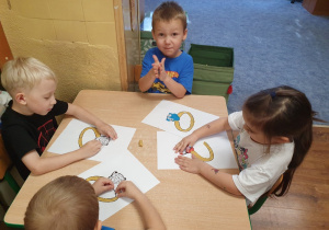 Dzieci wylepiają szablon pierścionka plasteliną i błyszczącymi koralikami.