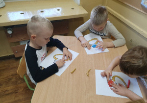 Dzieci wylepiają szablon pierścionka plasteliną i błyszczącymi koralikami.