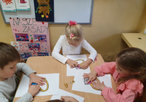 Dzieci wylepiają szablon pierścionka plasteliną i błyszczącymi koralikami.