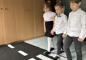 Dzieci przechodzą przez rozłożona matę obrazującą przejście dla pieszych.