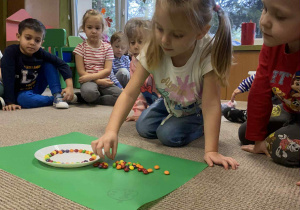 dziewczynka układa kolorowe cukierki na talerzyku z wodą