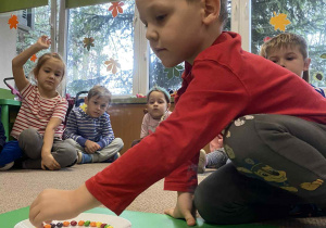 chłopiec układa kolorowe cukierki na talerzyku z wodą