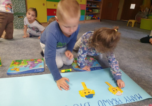 Dzieci przyklejają uśmiechnięte buźki tworząc plakat.