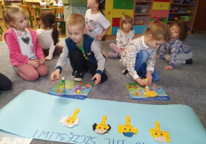 Dzieci przyklejają uśmiechnięte buźki tworząc plakat.