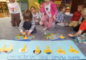 Dzieci przyklejają uśmiechnięte twarze tworząc plakat.