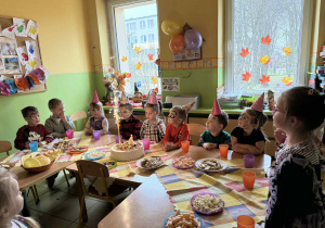 Dzieci siedzą przy stolikach podczas poczęstunku.