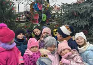 Dzieci w parku ubierają świąteczne drzewko.