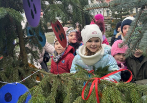 Dzieci w parku ubierają świąteczne drzewko.