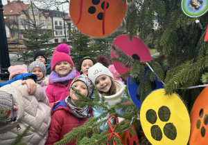 Dzieci w parku ubierają świąteczne drzewko.