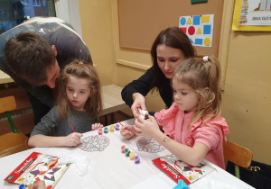 Dzieci malują ozdoby wspólnie z rodzicami.