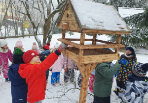 Dzieci wsypują ziarna do karmnika.