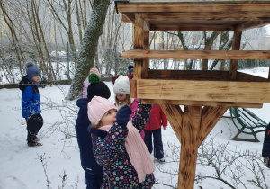Dzieci wsypują ziarna do karmnika.