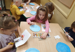 Dzieci wykonują pracę plastyczną - malowanie farbą i wycinanie.