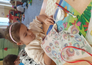 Dziewczynka ozdabia zakładkę do książki metodą decoupage.
