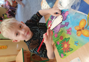 Chłopiec ozdabia zakładkę do książki metodą decoupage.