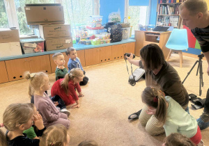 Dzieci słuchają i oglądają sprzęt fotograficzny.