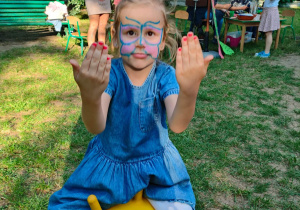 Dziewczynka skacze na gumowej piłce i prezentuje pomalowane na pikniku paznokcie.