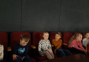 Dzieci siedzą na fotelach i oglądają film.