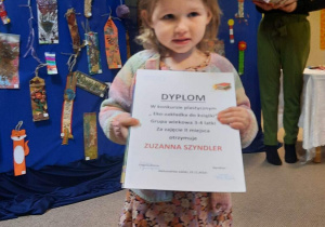 Dziewczynka trzyma dyplom i nagrodę książkową.