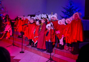 Dzieci z grupy siódmej w czerwonych peleryach śpiewją kolęde