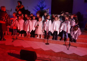 Dzieci z grupy szóstej białych pelerynach śpiewają kolęde
